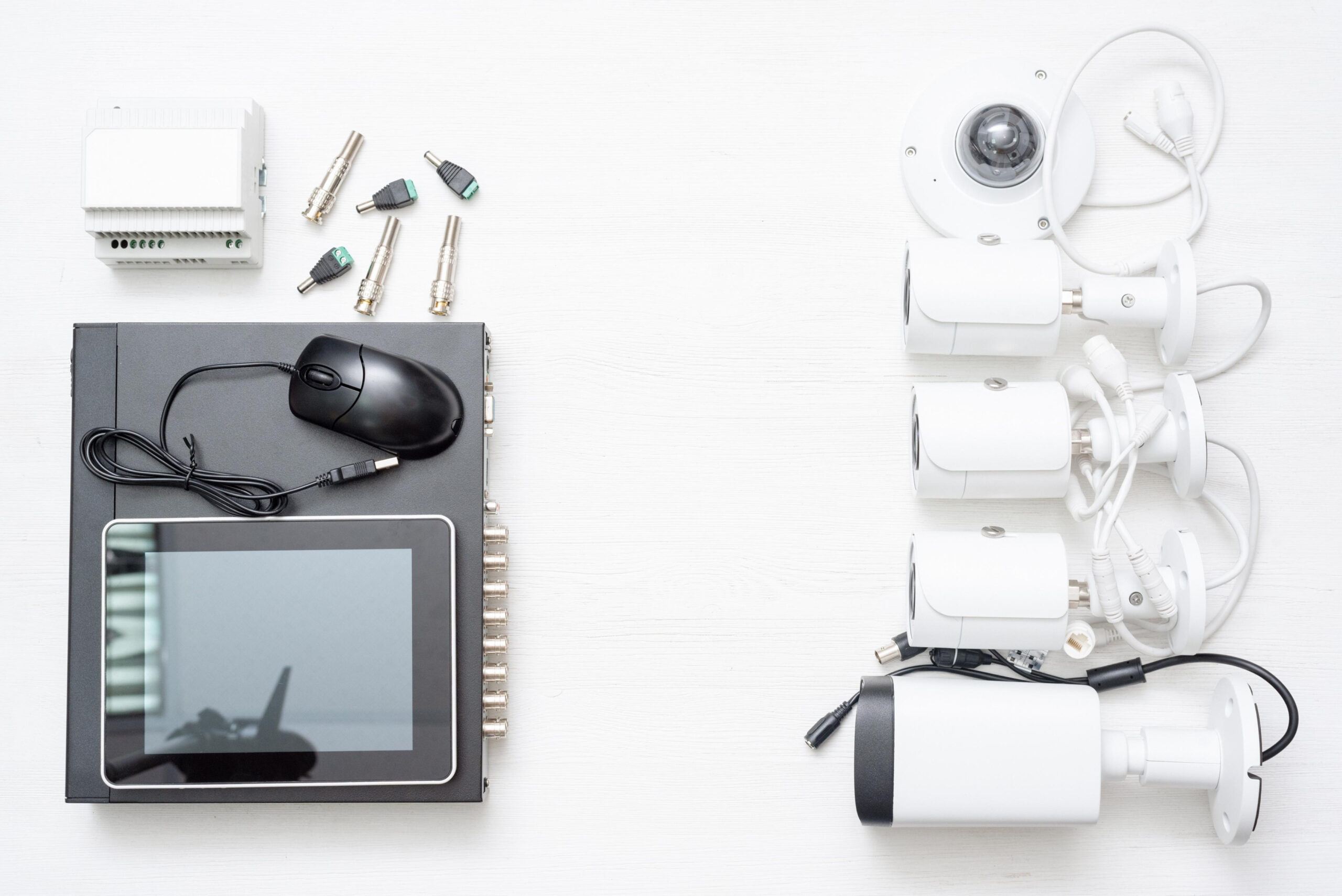Security camera setup, cctv installation A complete CCTV security system laid out on a white surface, including multiple white bullet cameras, a dome camera, connectors, a DVR unit with a mouse, and various cables.