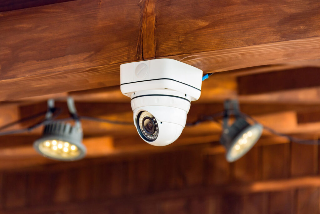 A white dome-style security camera mounted on a wooden ceiling with two LED lights nearby.