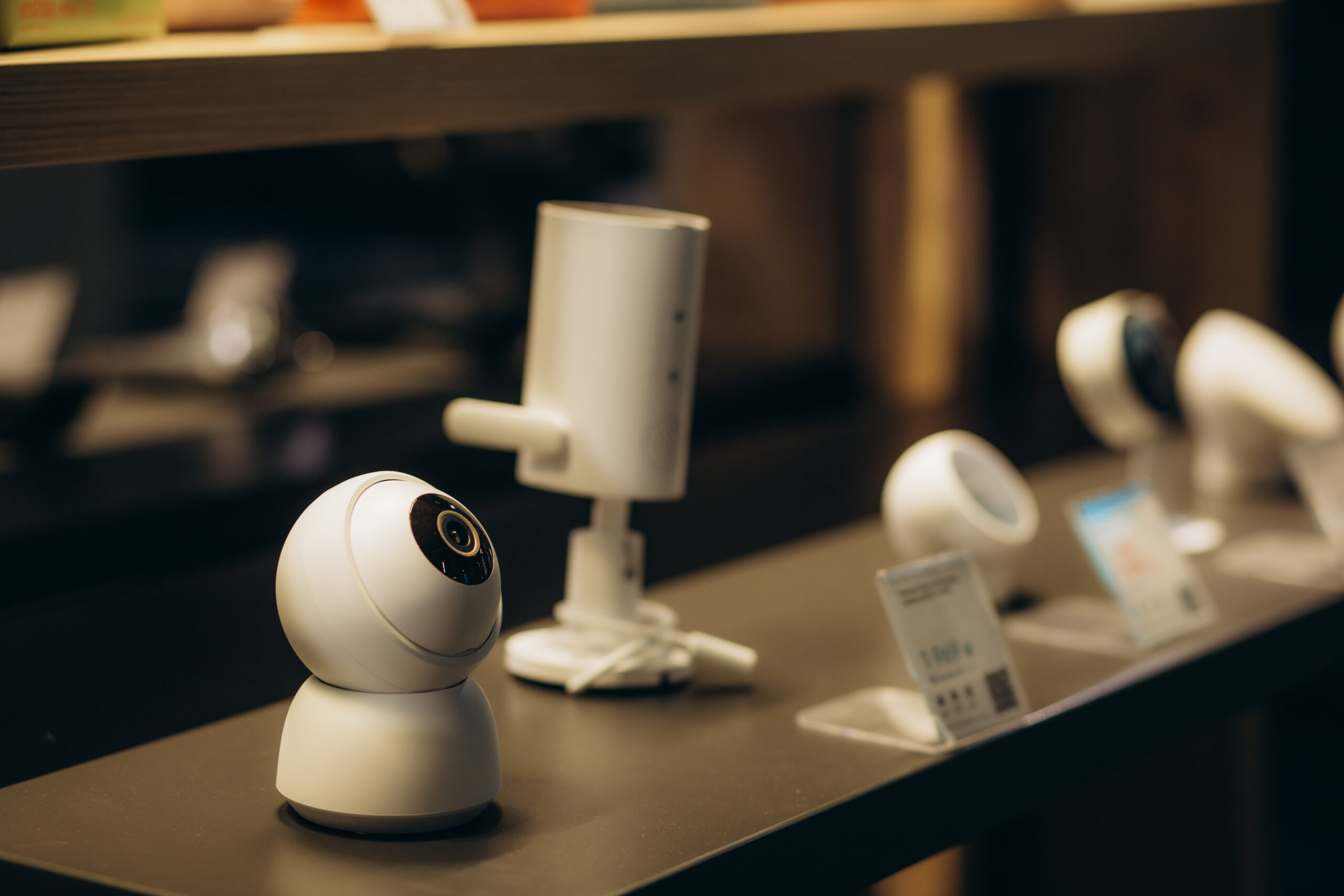 web cameras on display in an electronics store A row of modern smart security cameras on display in an electronics store, arranged on a counter with price tags in front of them.