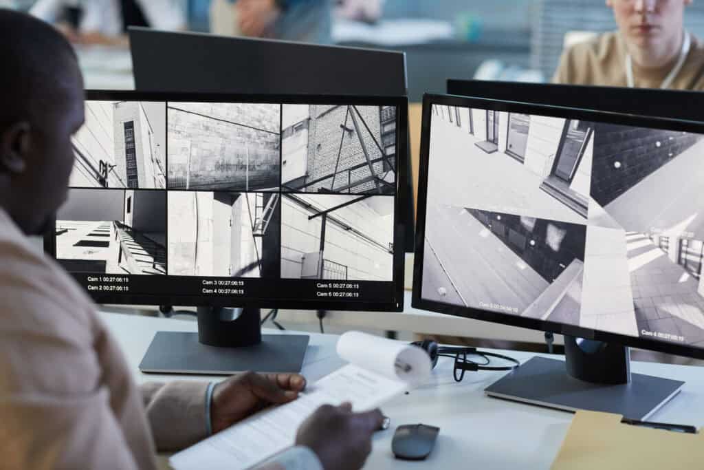 Security professional reviewing surveillance camera footage across multiple monitors in a monitoring center.